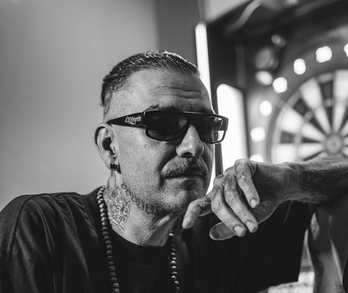 Retrato en blanco y negro de un hombre con gafas de sol y tatuajes.