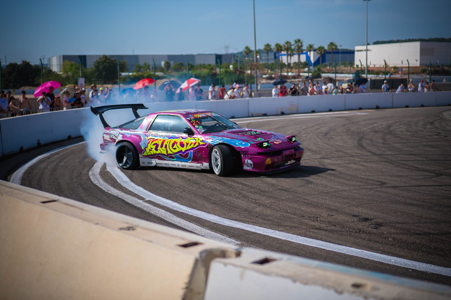 Coche de drift rosa derrapando en un circuito ante el público.