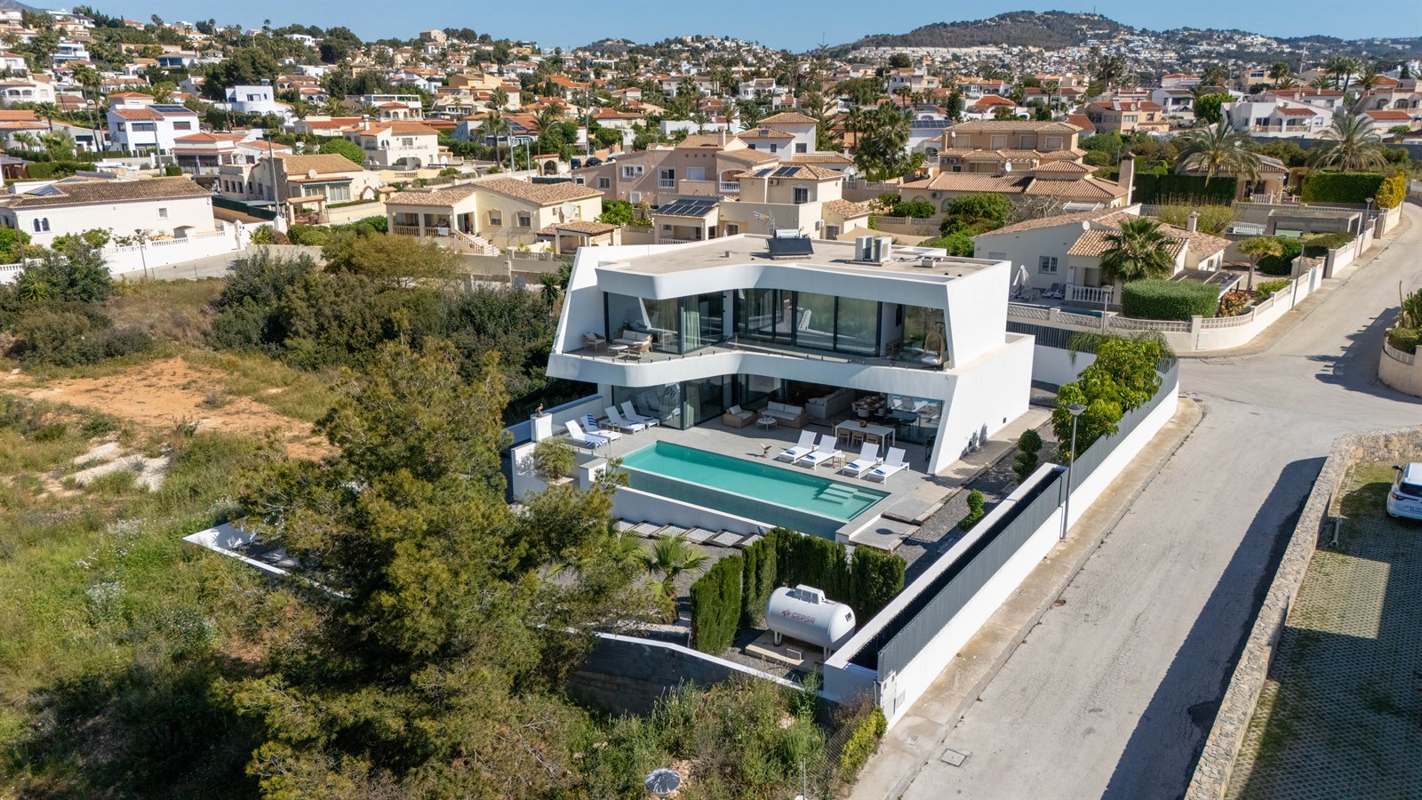 Vista aérea oblicua de una villa blanca contemporánea con piscina y grandes ventanales.