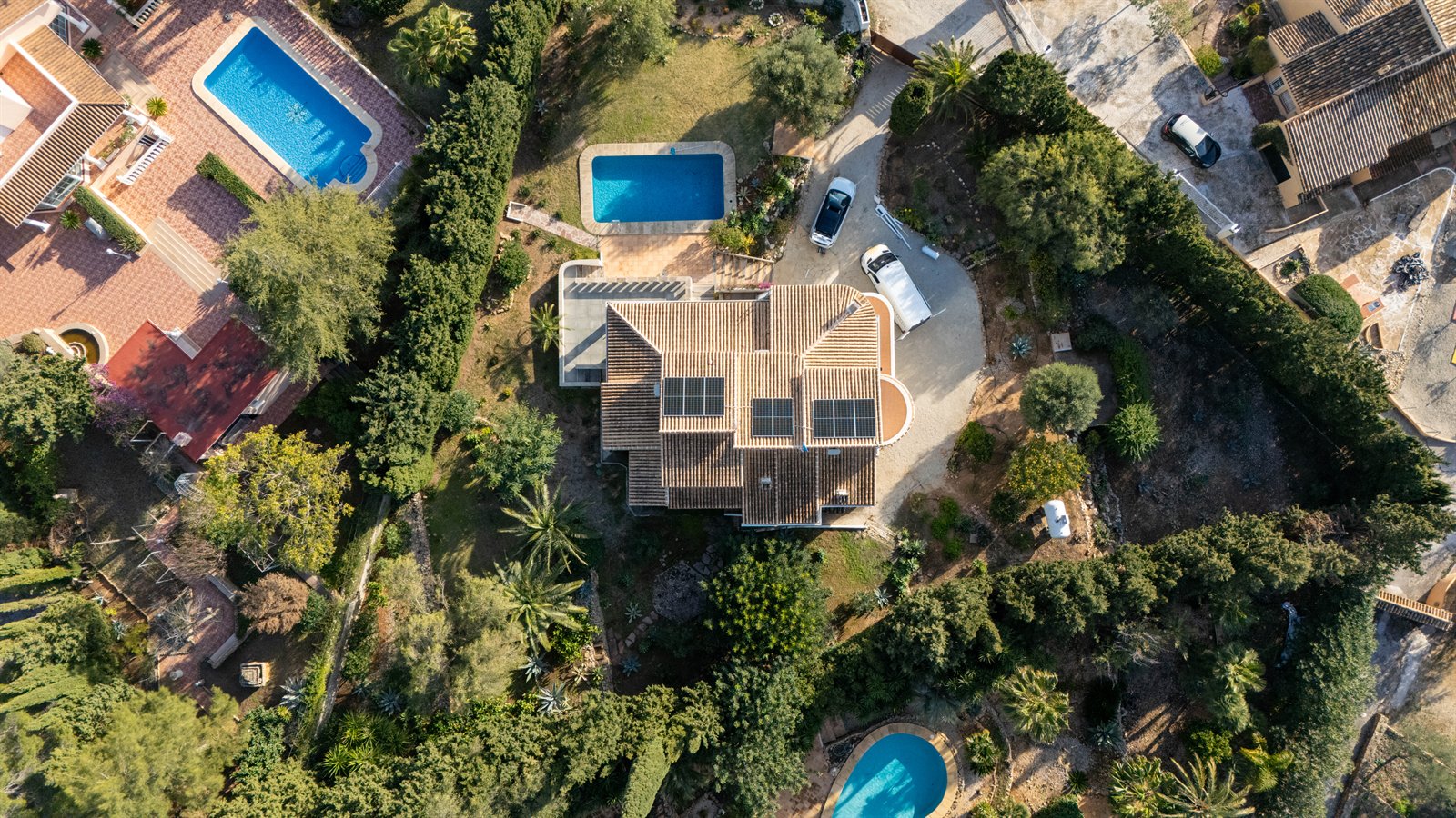 Vista cenital de una vivienda rodeada de jardines, árboles y piscinas.