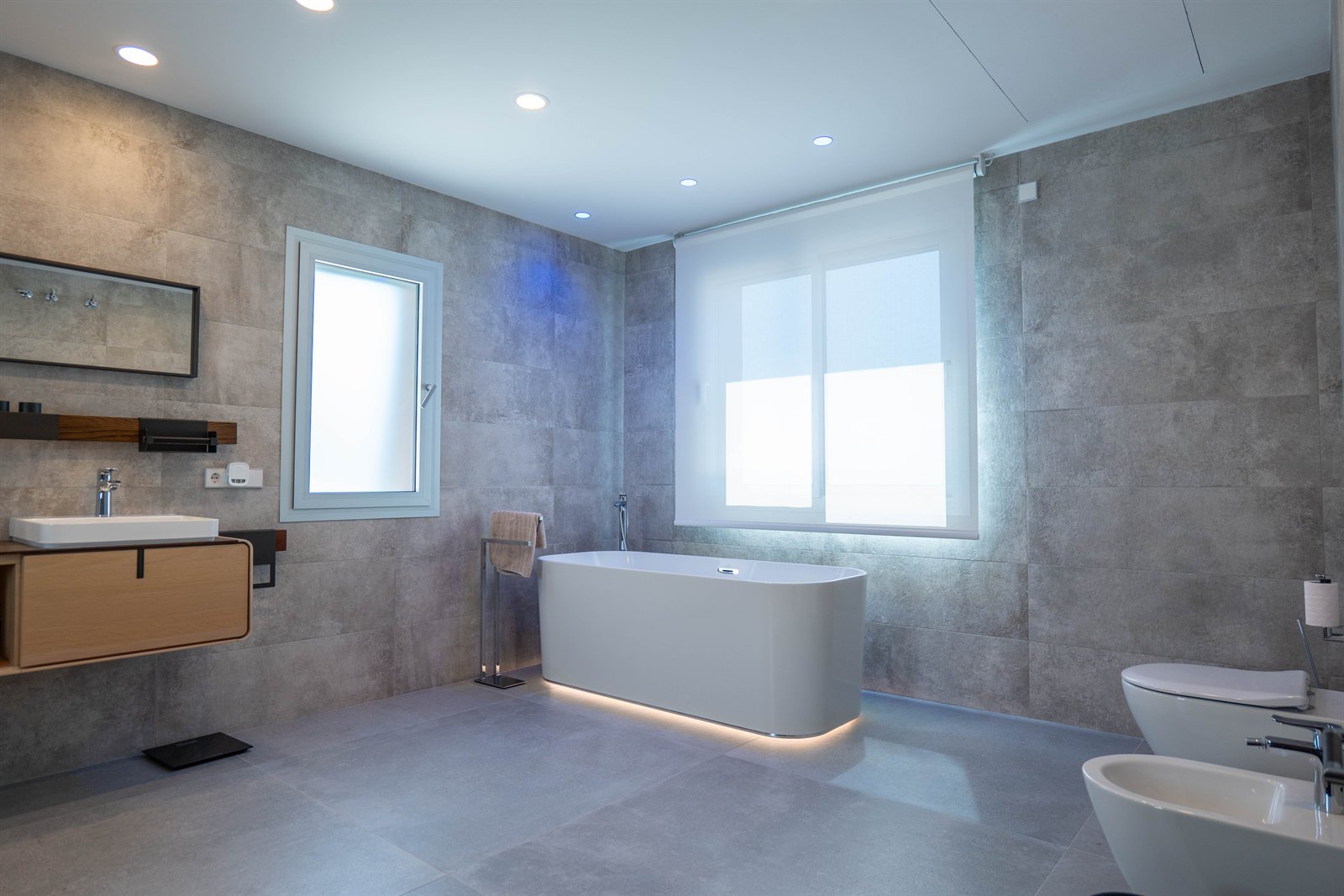 Baño contemporáneo de tonos grises con bañera exenta y mobiliario de madera.