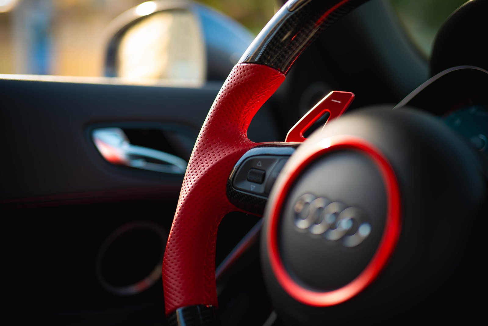 Detalle de un volante deportivo de cuero rojo iluminado por la luz lateral.