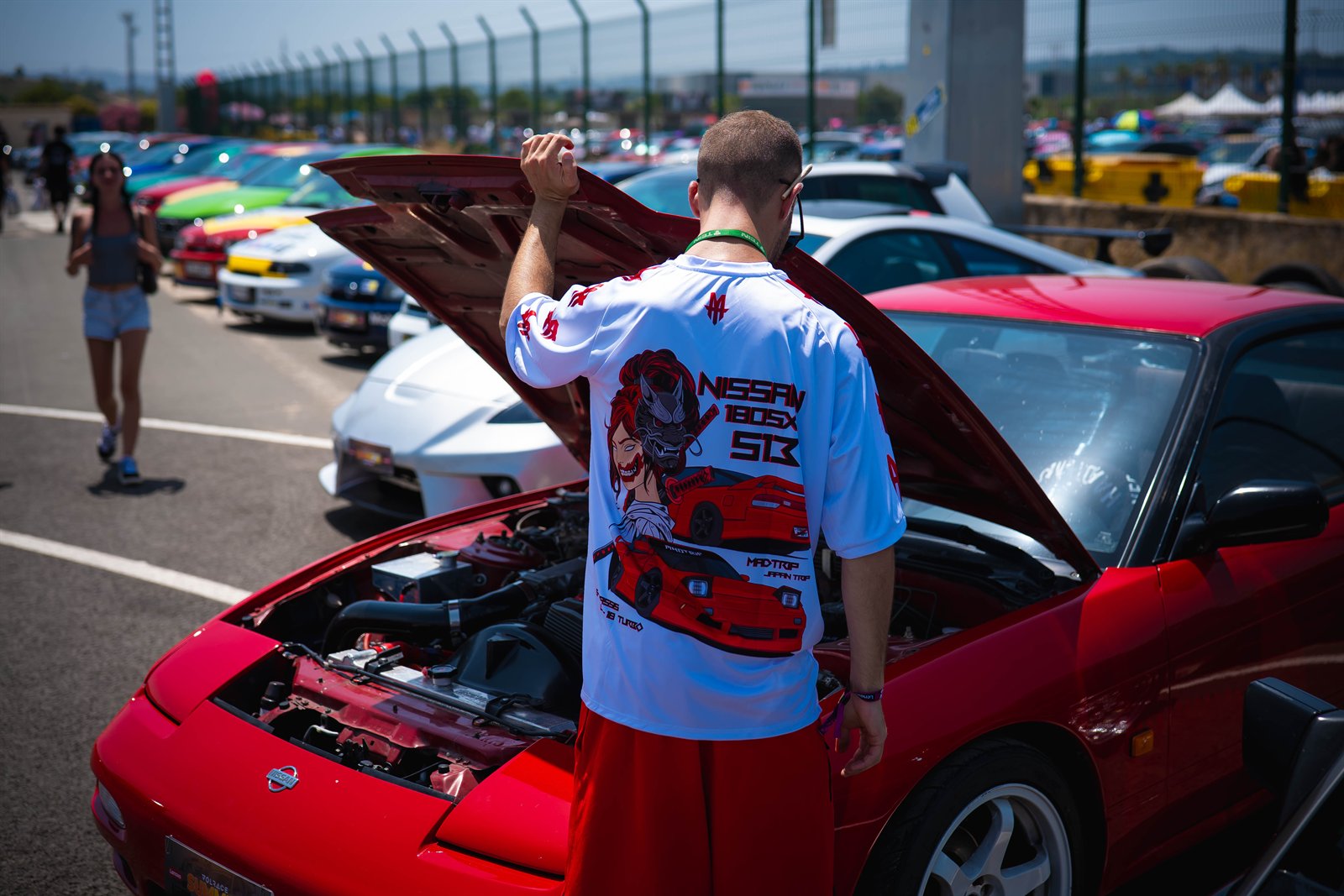 Asistente levantando el capó de un coche rojo en una exposición de vehículos.