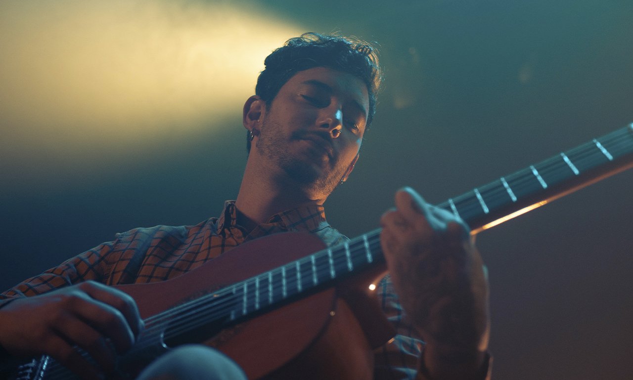 Guitarrista tocando en directo bajo luces azules y cálidas.