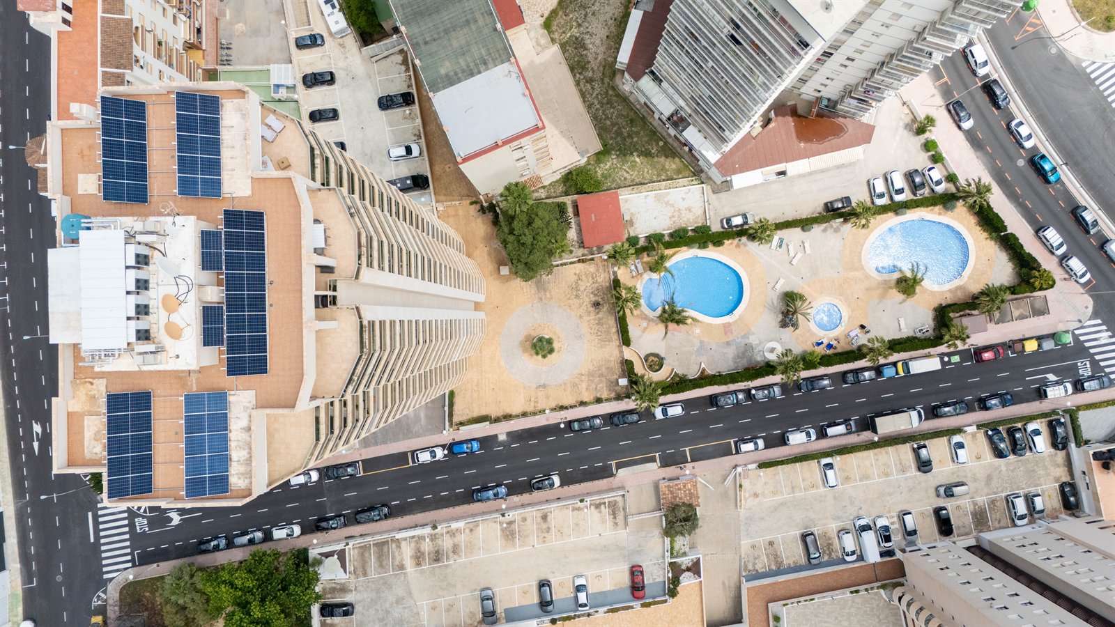 Vista cenital de edificios, piscinas, calles y coches desde gran altura.