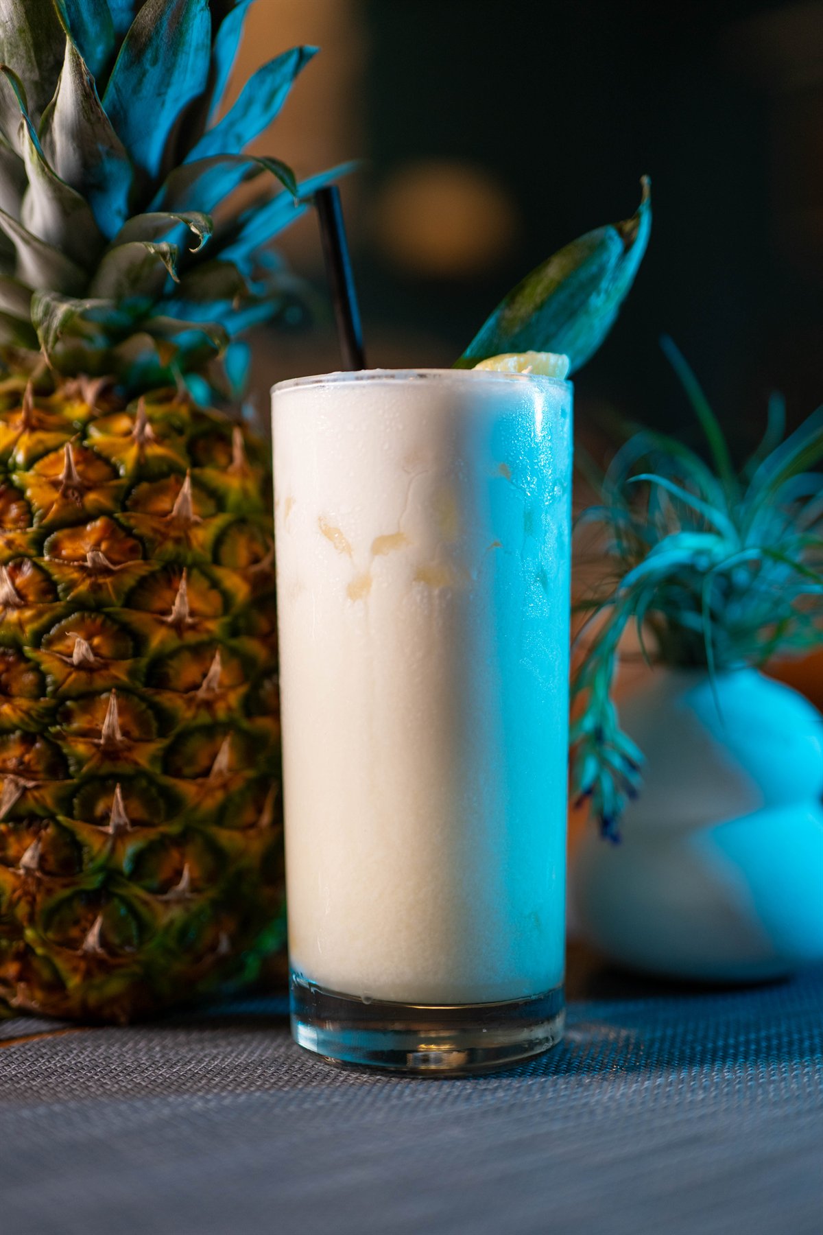 Cóctel cremoso servido junto a una piña bajo iluminación azul.