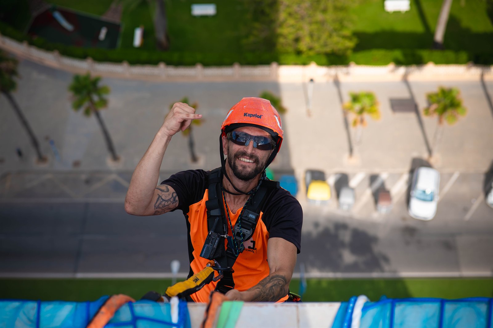 Trabajador con casco y arnés suspendido ante una vista urbana desde gran altura.