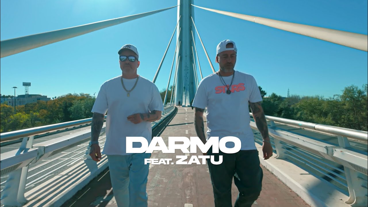 Darmo y Zatu caminando sobre un puente moderno bajo un cielo azul.