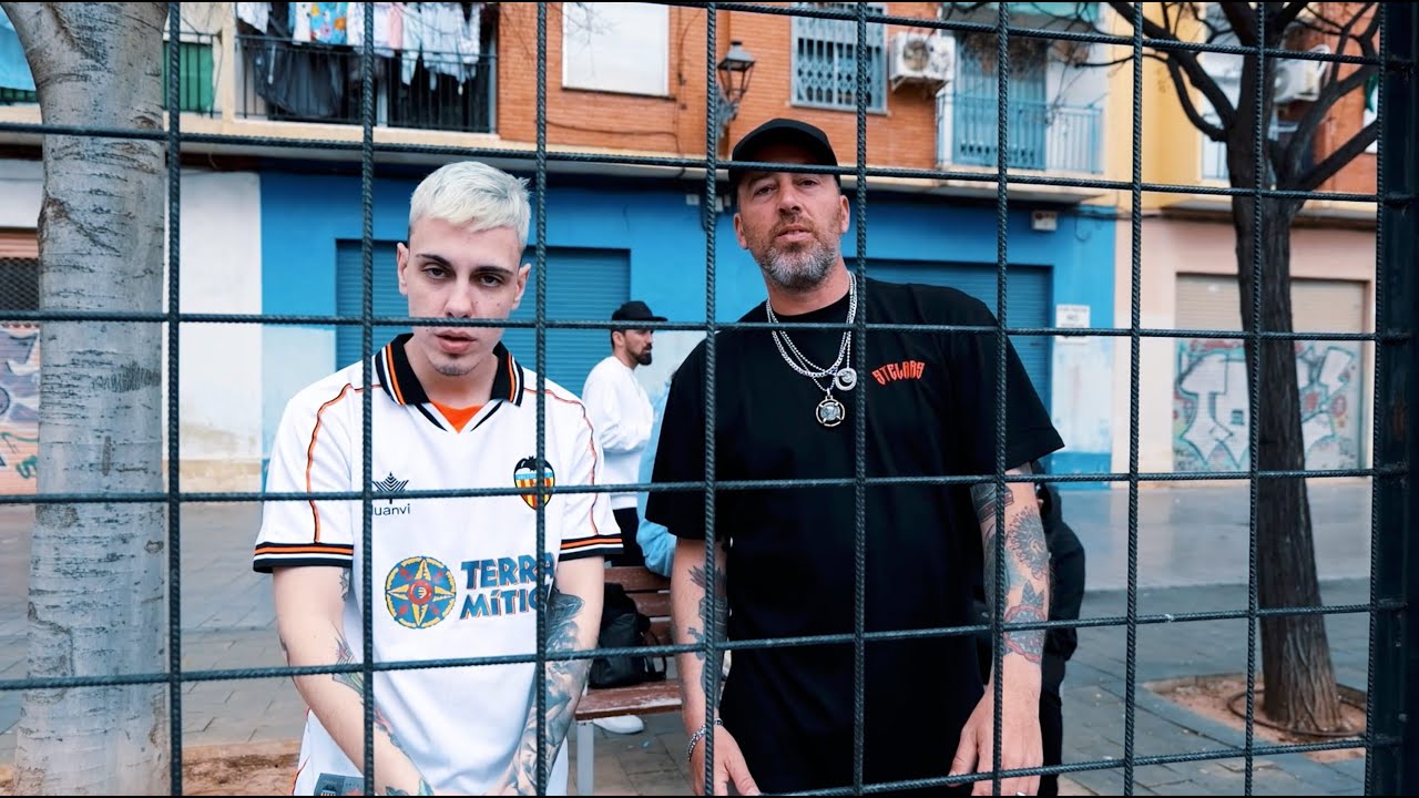 Dos hombres frente a una valla metálica en una calle urbana.