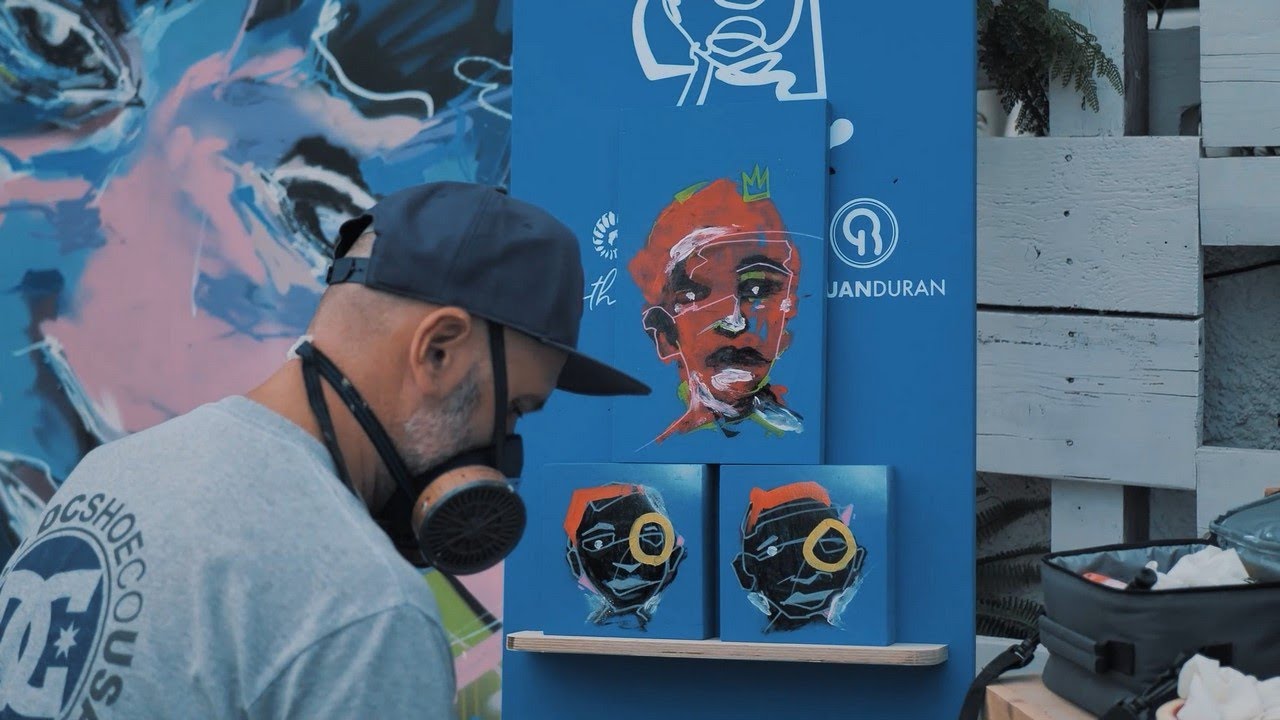 Artista trabajando junto a varias pinturas de retratos de colores.